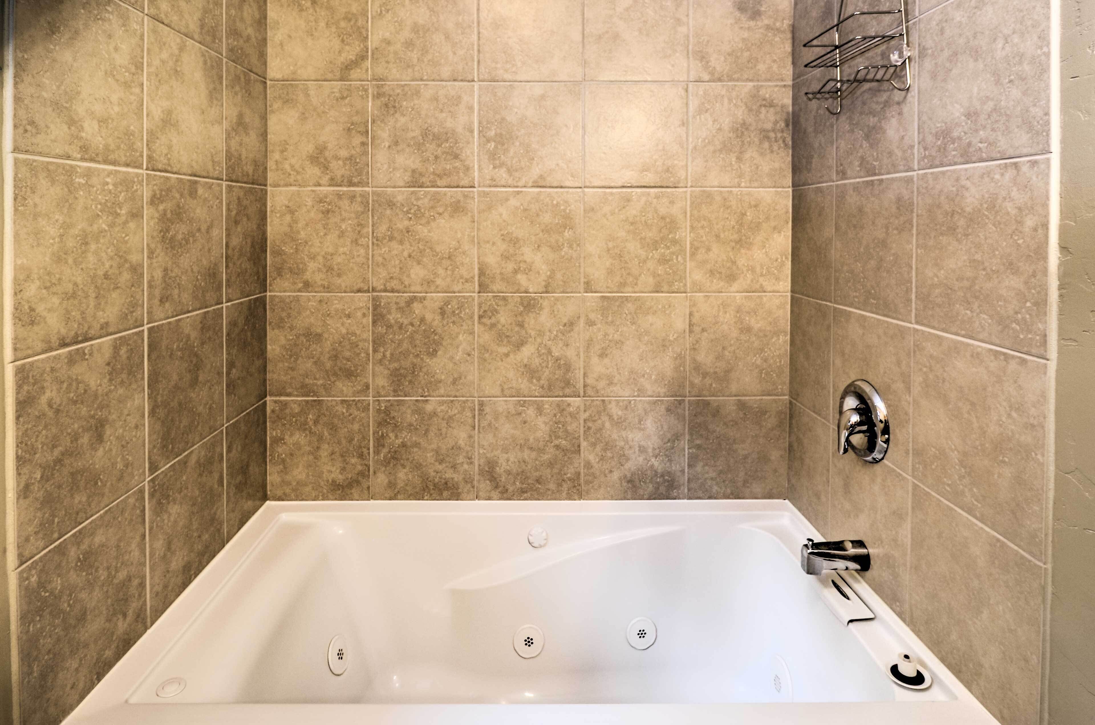 A bathroom with a white bathtub, beige tiles, and a chrome faucet.