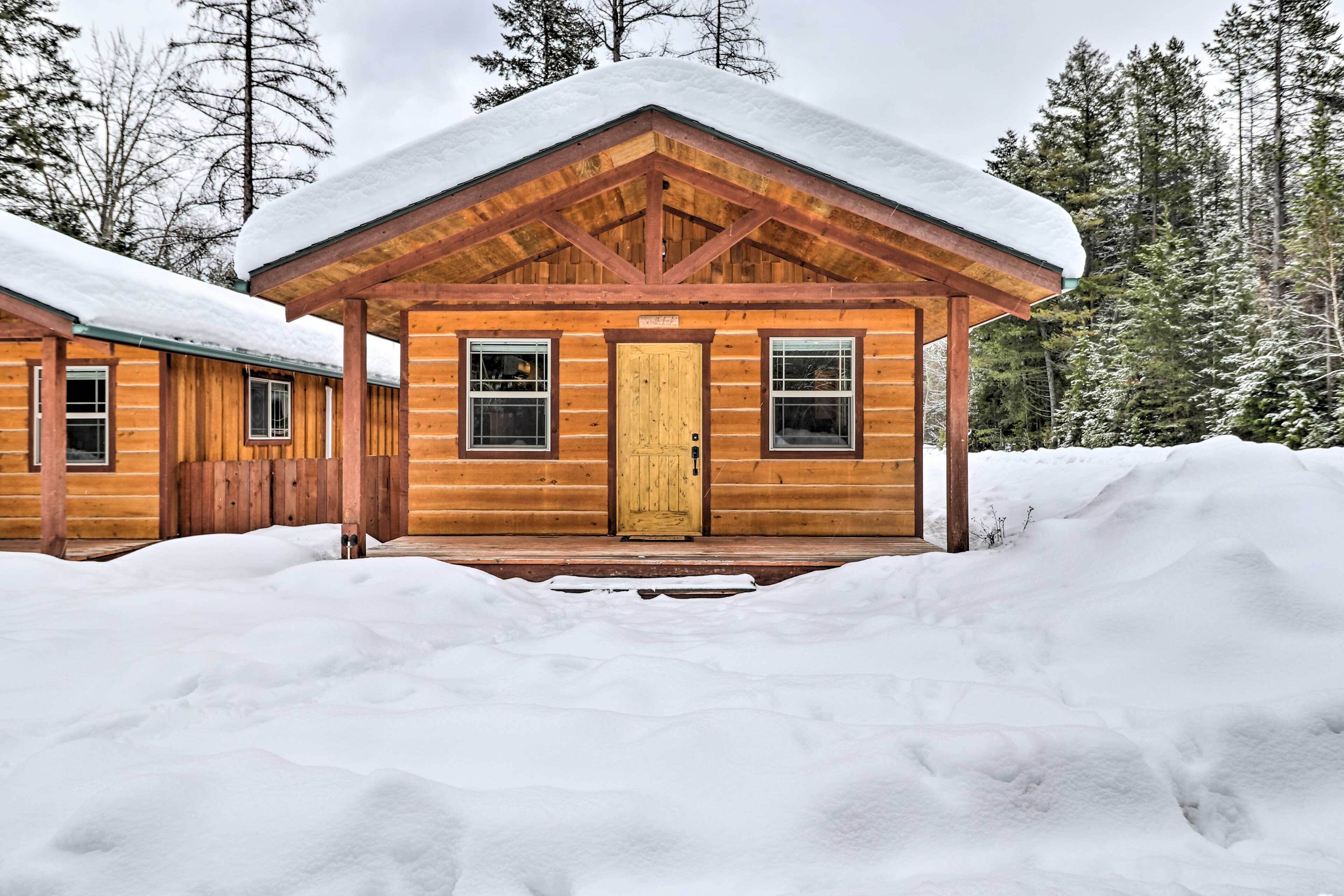 A wooden cabin with a snow-covered roof and a wooden door, surrounded by snow and trees.