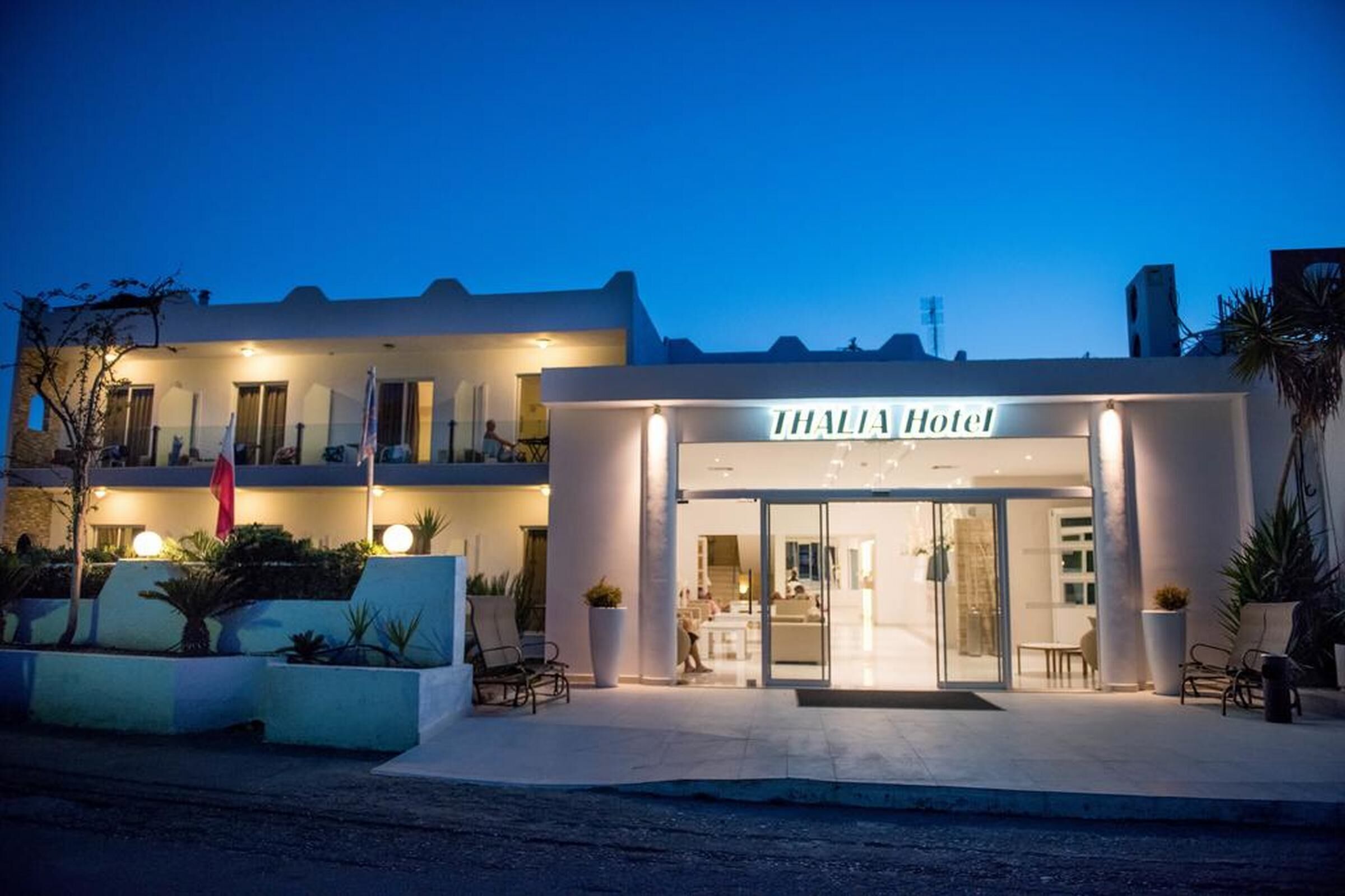 A hotel entrance with a glass door, a sign reading "THALIA Hotel", and a balcony with seating.