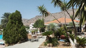 A poolside area with outdoor seating, a mountain backdrop, and a building with a red-tiled roof. - Thalia Hotel (Rhodes)