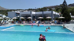 A pool area with lounge chairs and umbrellas, surrounded by buildings and hills. - Thalia Hotel (Rhodes)