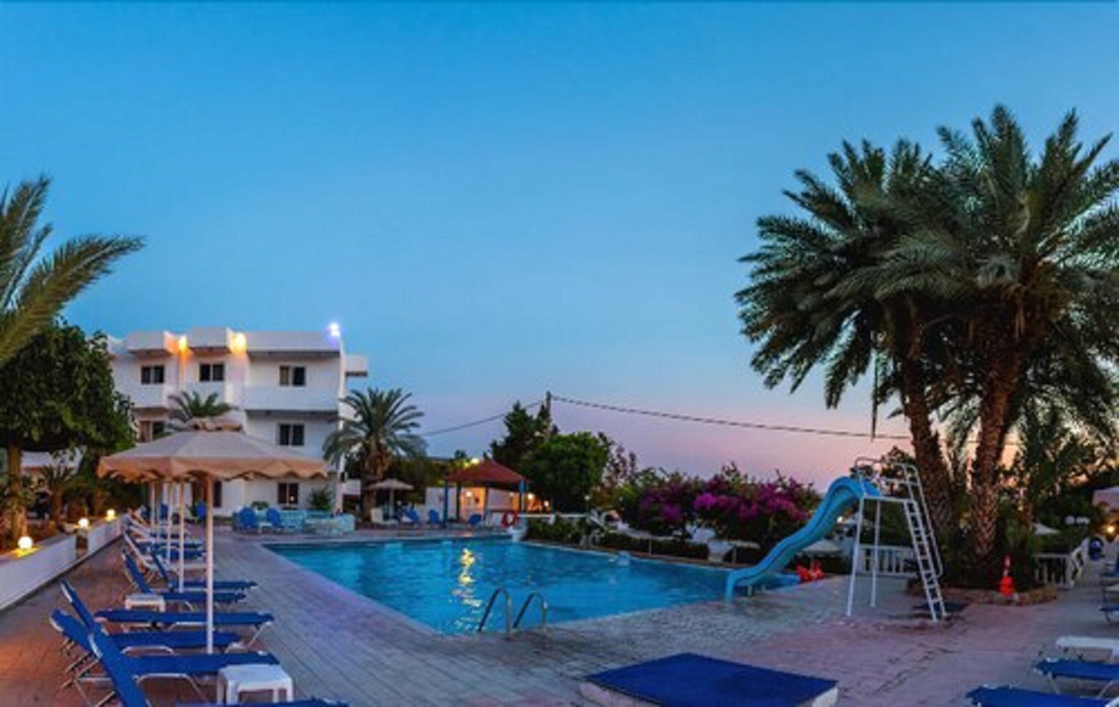A pool area with lounge chairs, a slide, and a building in the background.