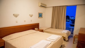 A hotel room with two beds, a wooden headboard, a bedside telephone, a window with curtains, and a view of the outside. - Thalia Hotel (Rhodes)