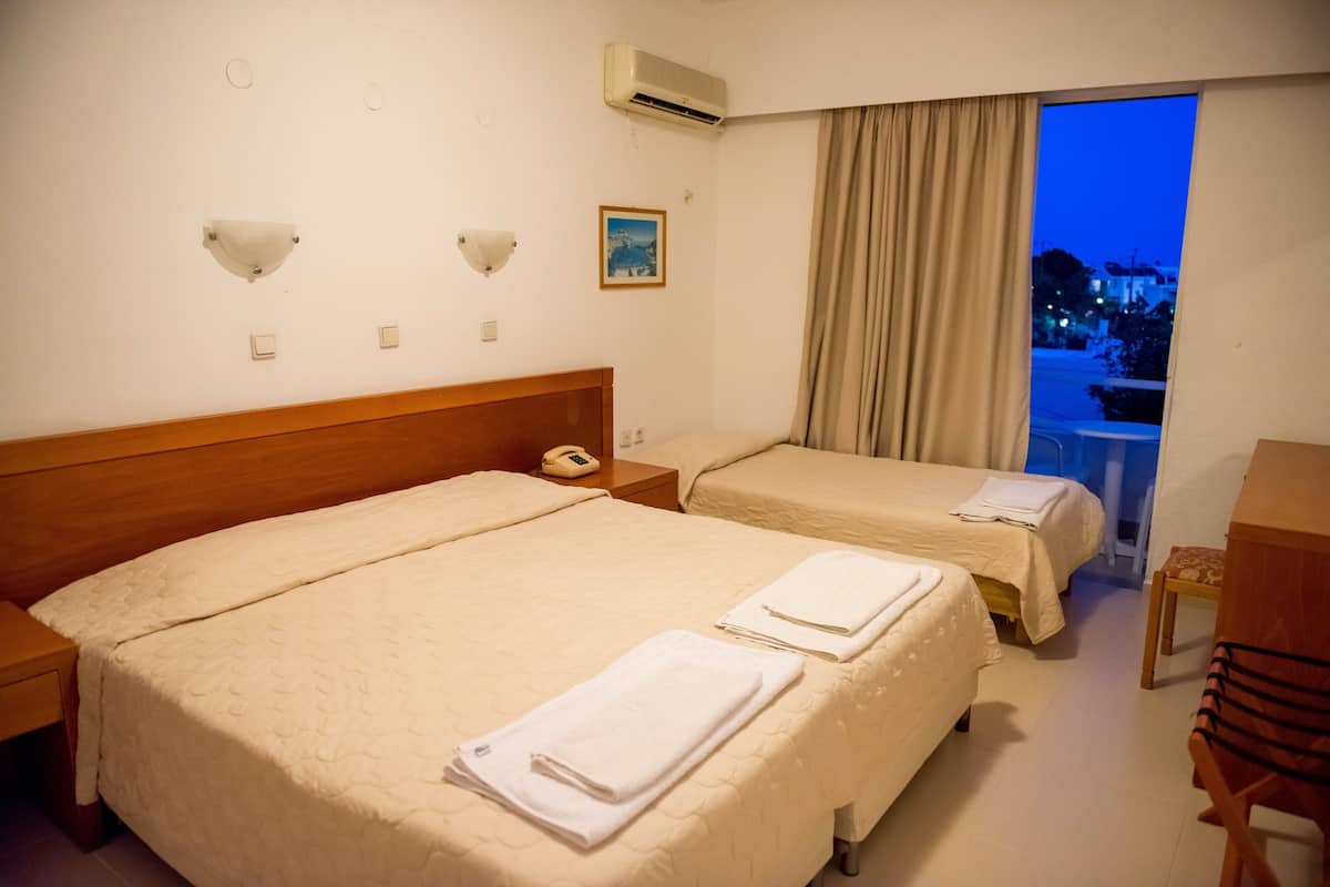A hotel room with two beds, a wooden headboard, a bedside telephone, a window with curtains, and a view of the outside.