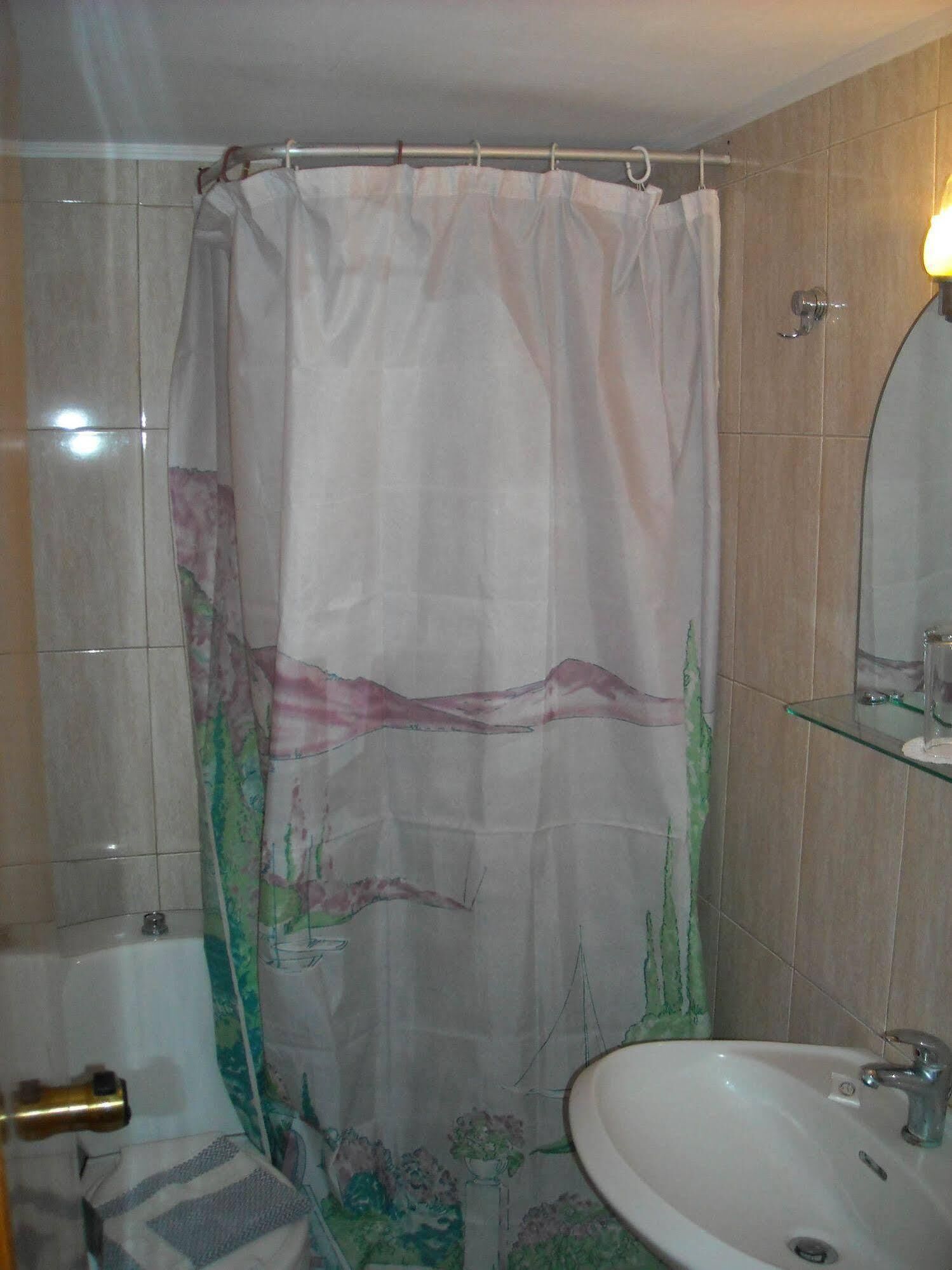 A bathroom with a shower curtain, a sink, a mirror, and a glass shelf.