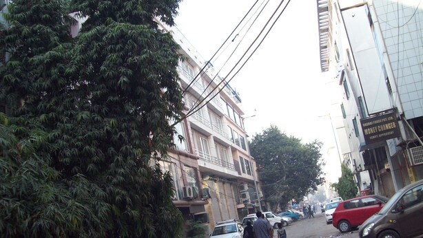 Vista de una calle con coches aparcados, edificios y gente caminando.