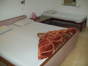 A room with two beds, one with a red blanket and the other with a white sheet. There is a small table with a pink object on it, and a wall-mounted heater. - Hotel Majors Den (New Delhi)