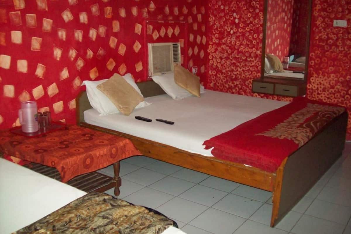 A bedroom with a bed, a bedside table, a mirror, and a red patterned wall.