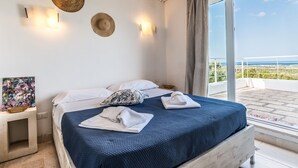 Ein Schlafzimmer mit Bett, Nachttisch, einem Gemälde und Blick aufs Meer.