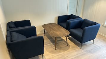 Une pièce dotée d’un plancher en bois, de murs recouverts de lambris blancs et de trois fauteuils bleu foncé disposés autour d’une table basse centrale en bois.