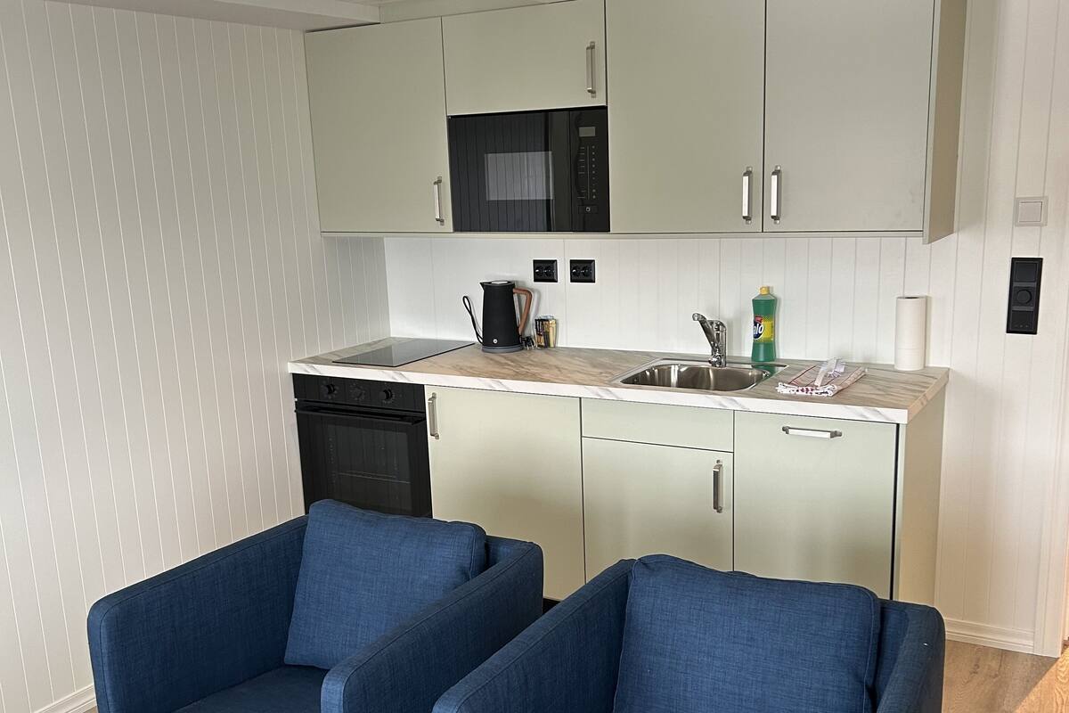 A compact living space with a kitchenette, two blue armchairs, and a small dining table.