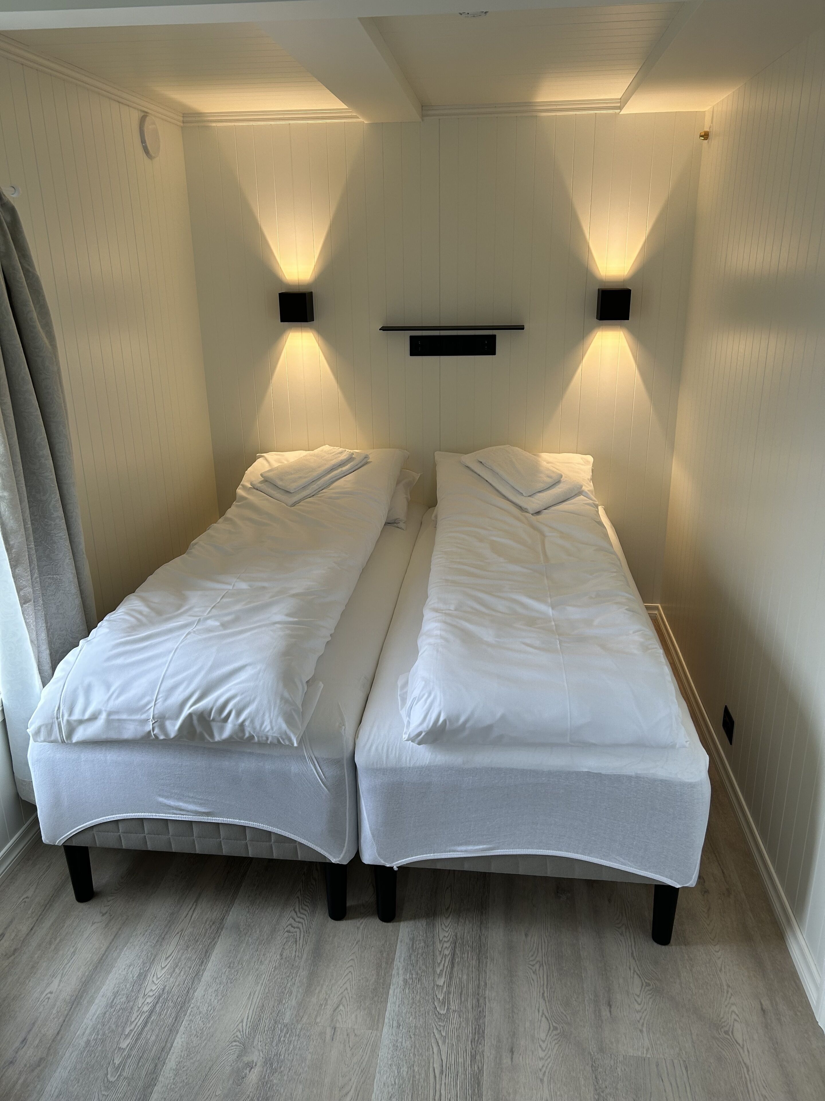 Una habitación con dos camas individuales, suelo de madera e iluminación en la pared.