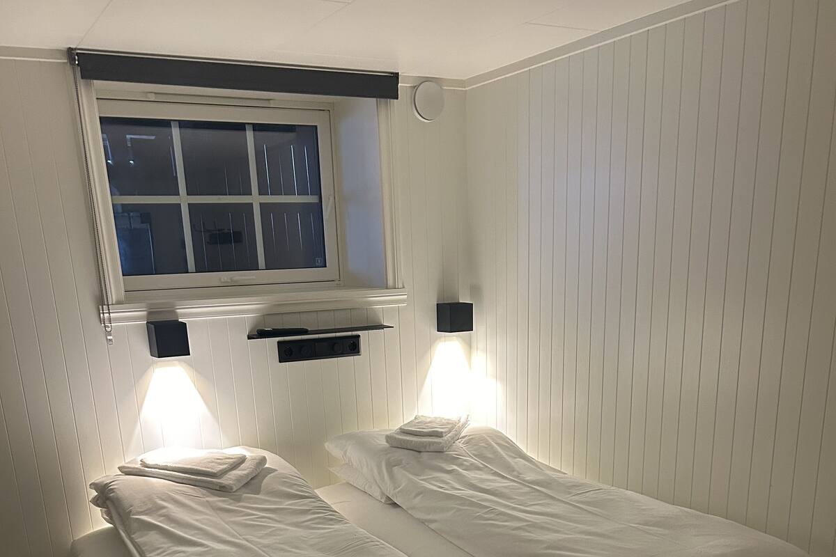 A twin room with two single beds, a window, a wall-mounted shelf, and two wall sconces.