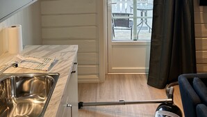 A modern kitchen with a stainless steel sink, a window with a view of a balcony, and a door with a curtain. - Finsnes Gaard (Senja)