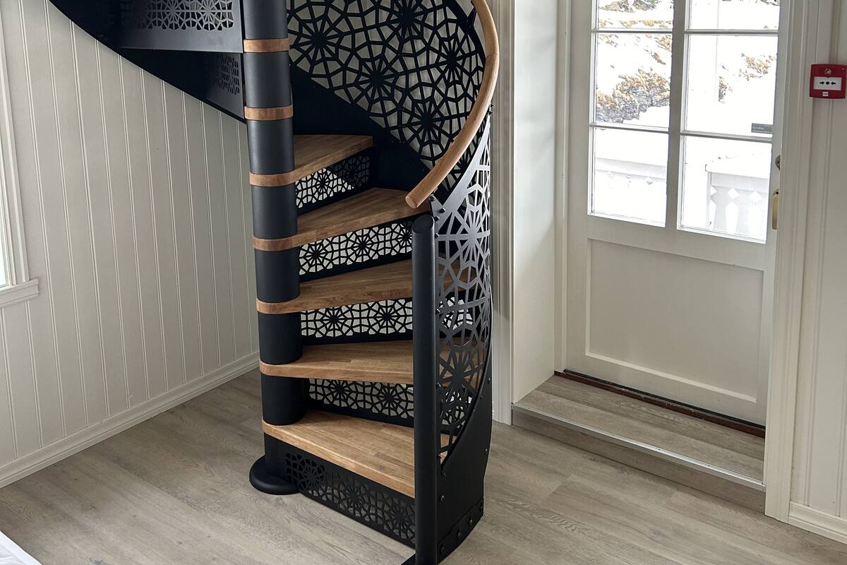 A spiral staircase with a wooden finish and black metal railings, leading to an upper floor.