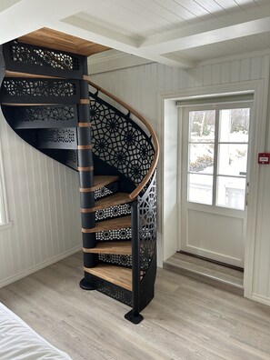 A spiral staircase with a wooden finish and black metal railings, leading to an upper floor.