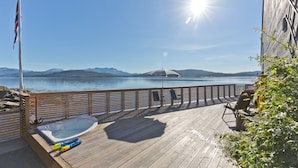 A wooden deck with a hot tub, chairs, and a flagpole. - Finsnes Gaard (Senja)