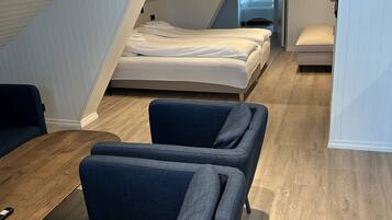 Een moderne, compacte kamer met een verhoogd bed, een klein zithoekje met banken, en een houten vloer.