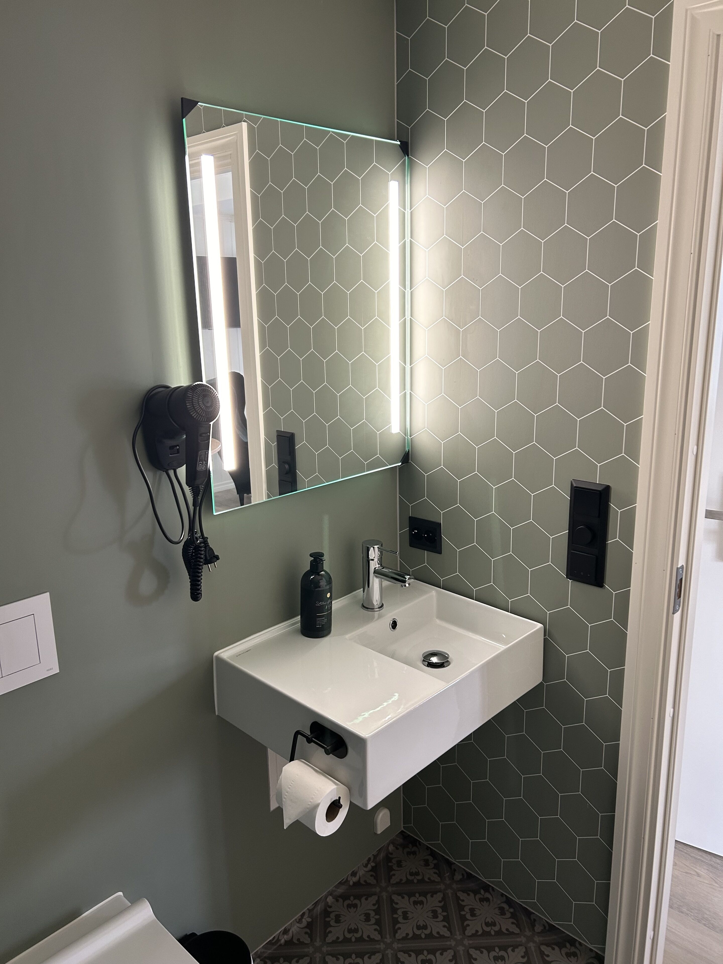 A bathroom with a white sink, a mirror, and a hexagonal patterned wall.