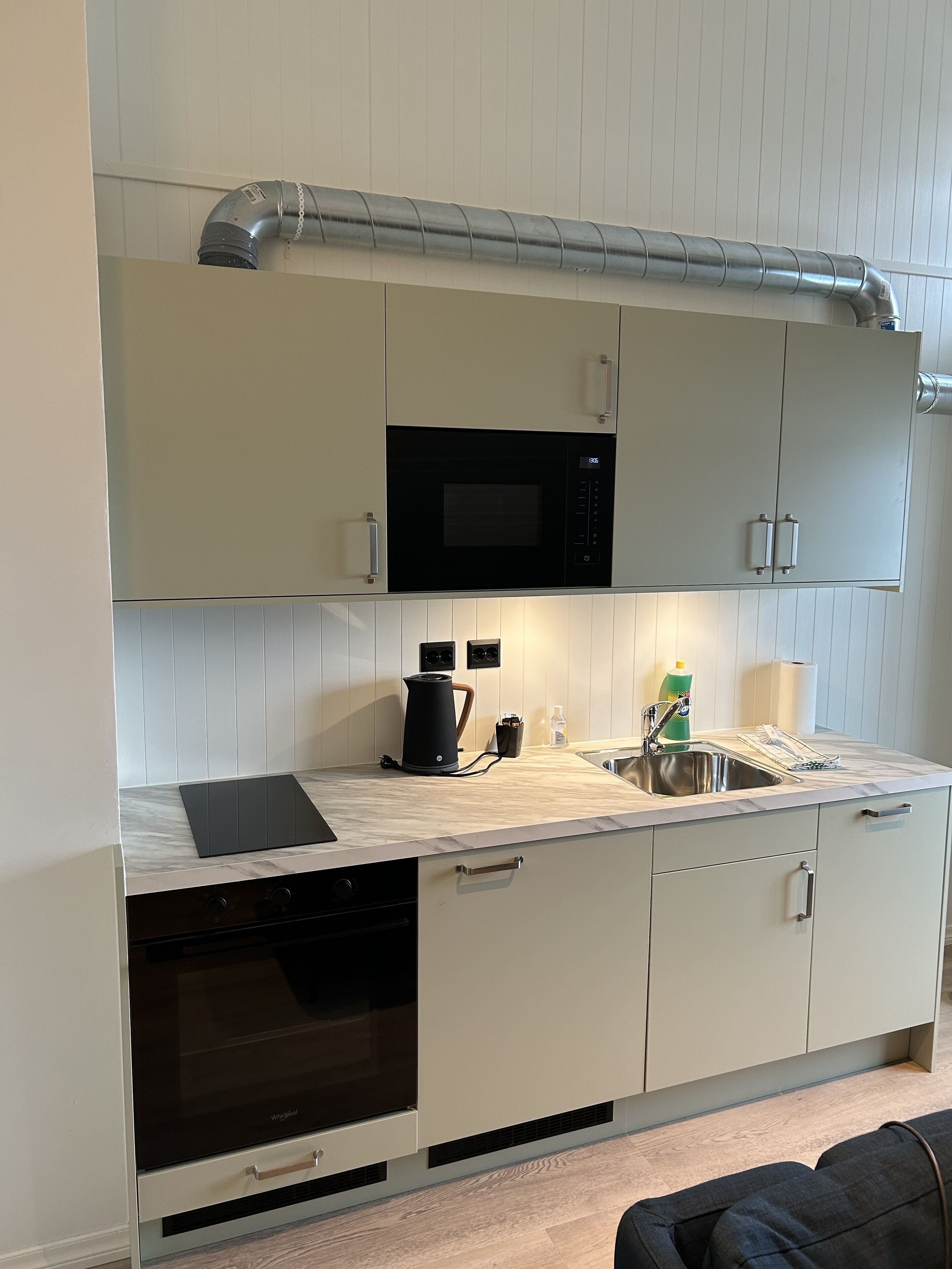 Een moderne keuken met witte kastjes, een ingebouwde magnetron, een waterkoker en een spoelbak.