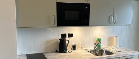 A modern kitchen with white cabinetry, a built-in microwave, a kettle, and a sink.