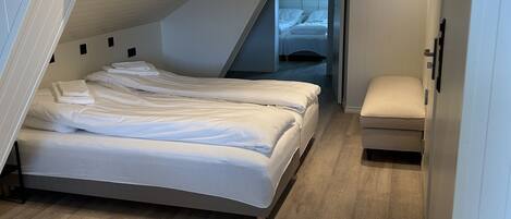 Een slaapkamer met een schuine kap, een bed, een bankje en een deur naar een andere kamer.