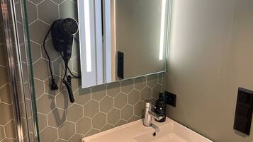 A bathroom with a white sink, a mirror with a light, and a hairdryer on the wall.