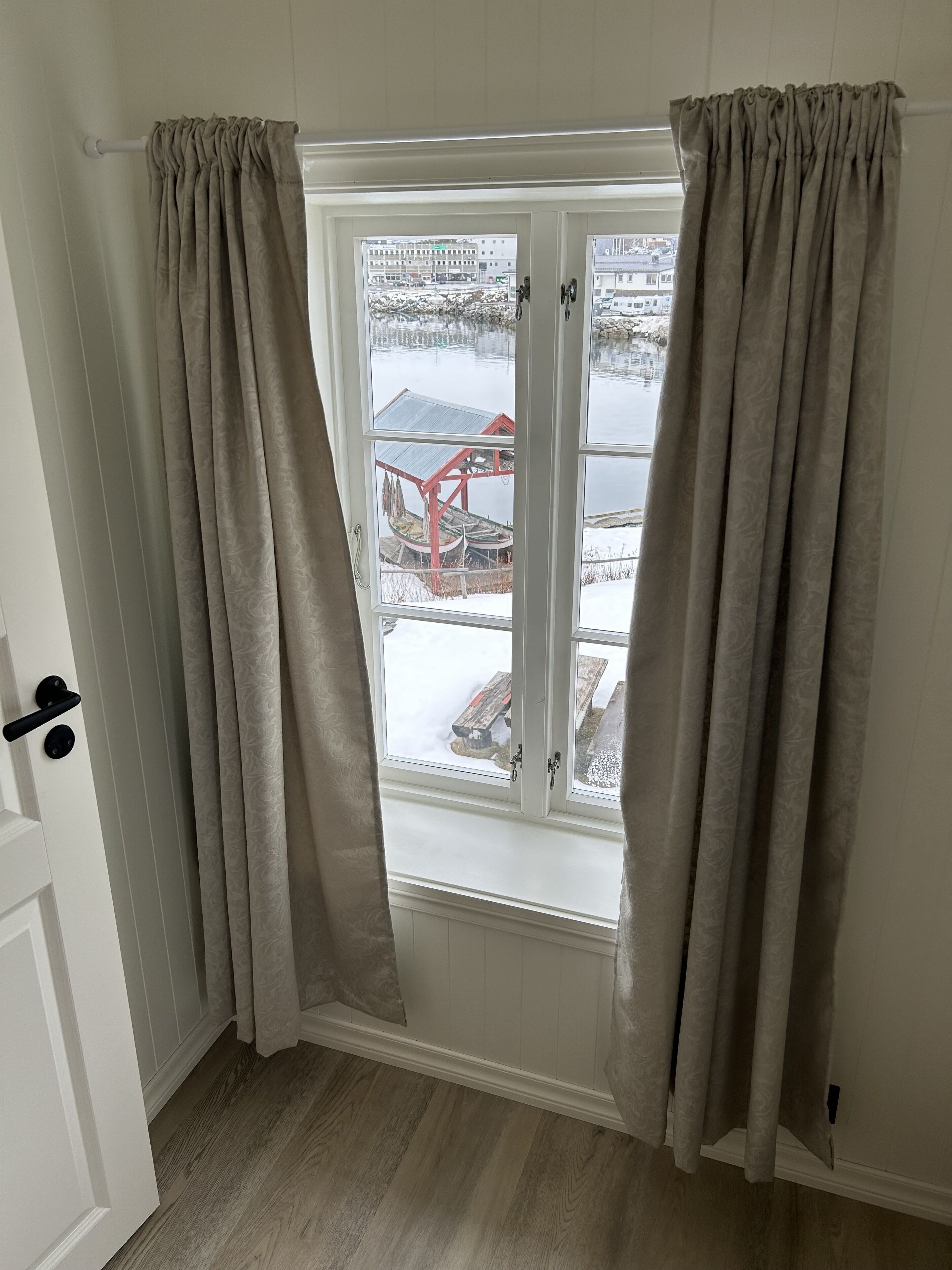 Een kamer met een raam dat uitkijkt op een besneeuwde omgeving, met een houten terras en een rode constructie.