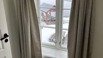 Een kamer met een raam dat uitkijkt op een besneeuwde omgeving, met een houten terras en een rode constructie.