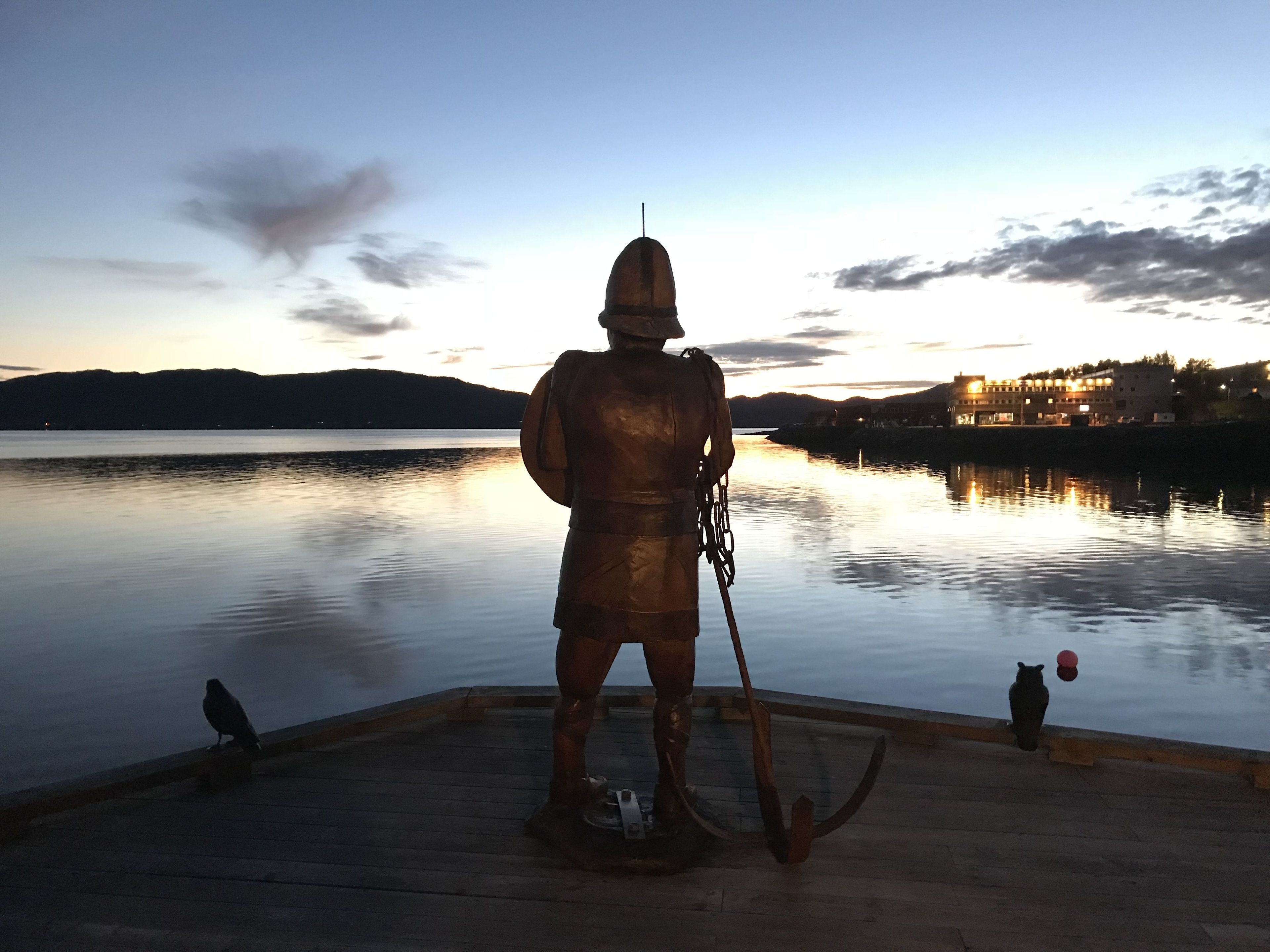 A statue of a knight on a dock with calm water and distant hills.