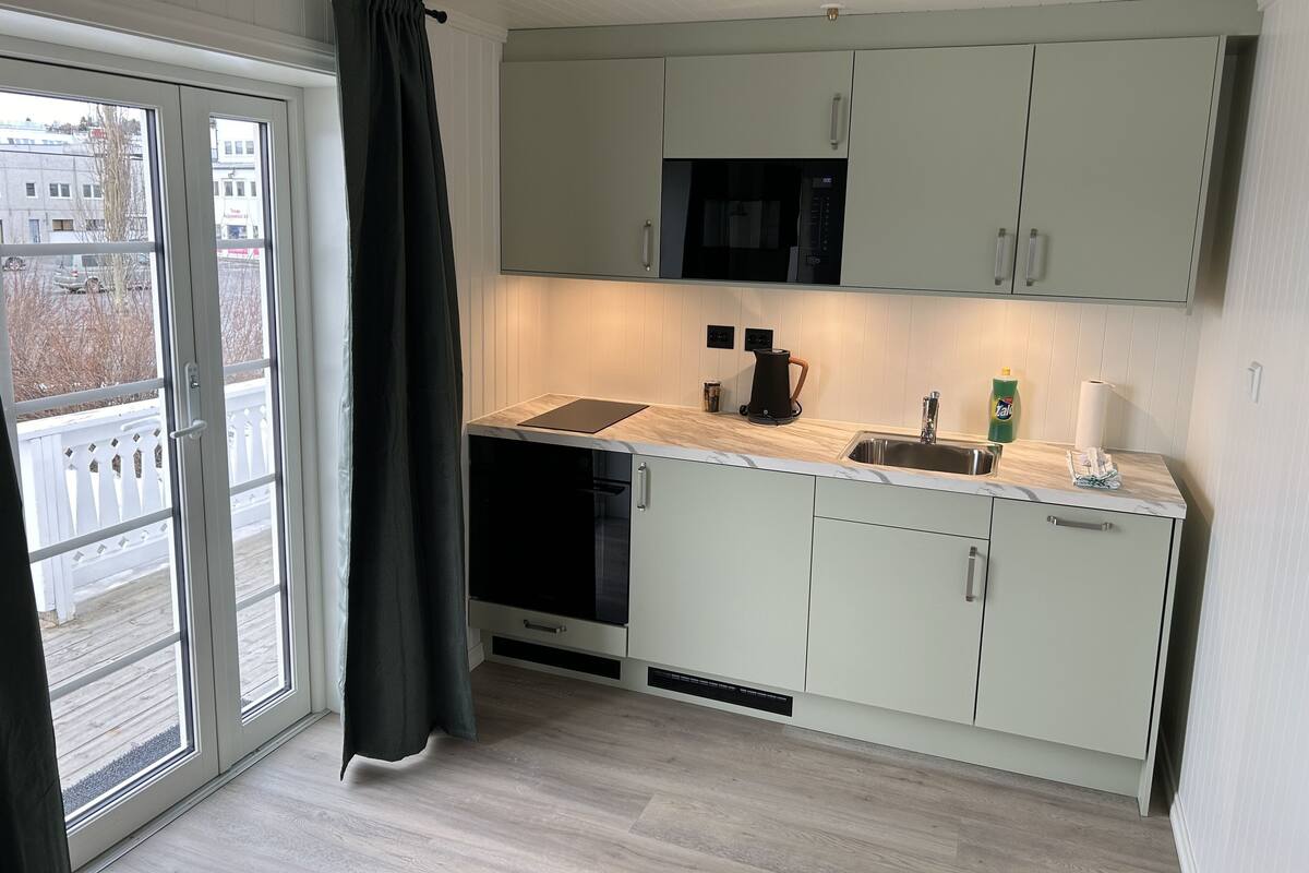 A modern kitchen with light green cabinets, a black microwave, a coffee maker, and a sink.