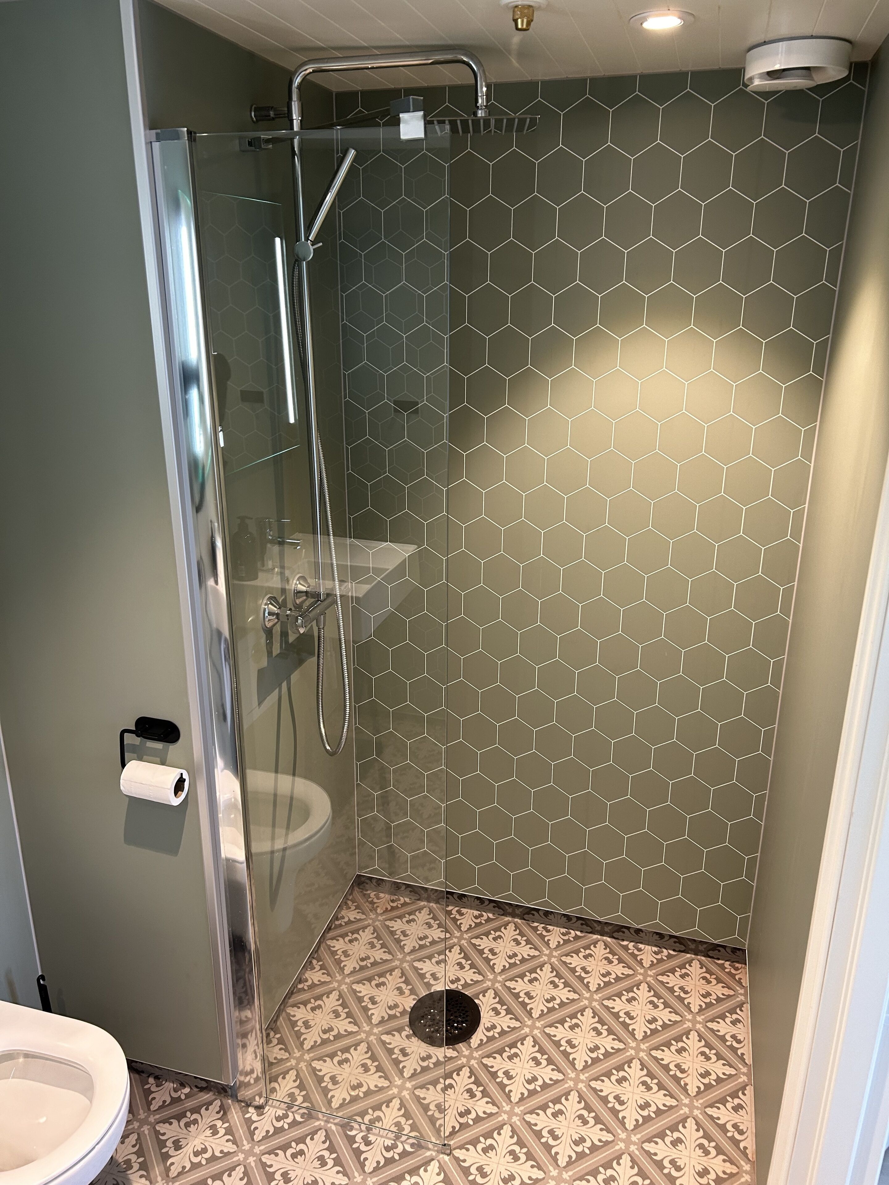 A shower with a glass door, a toilet, and a patterned floor.