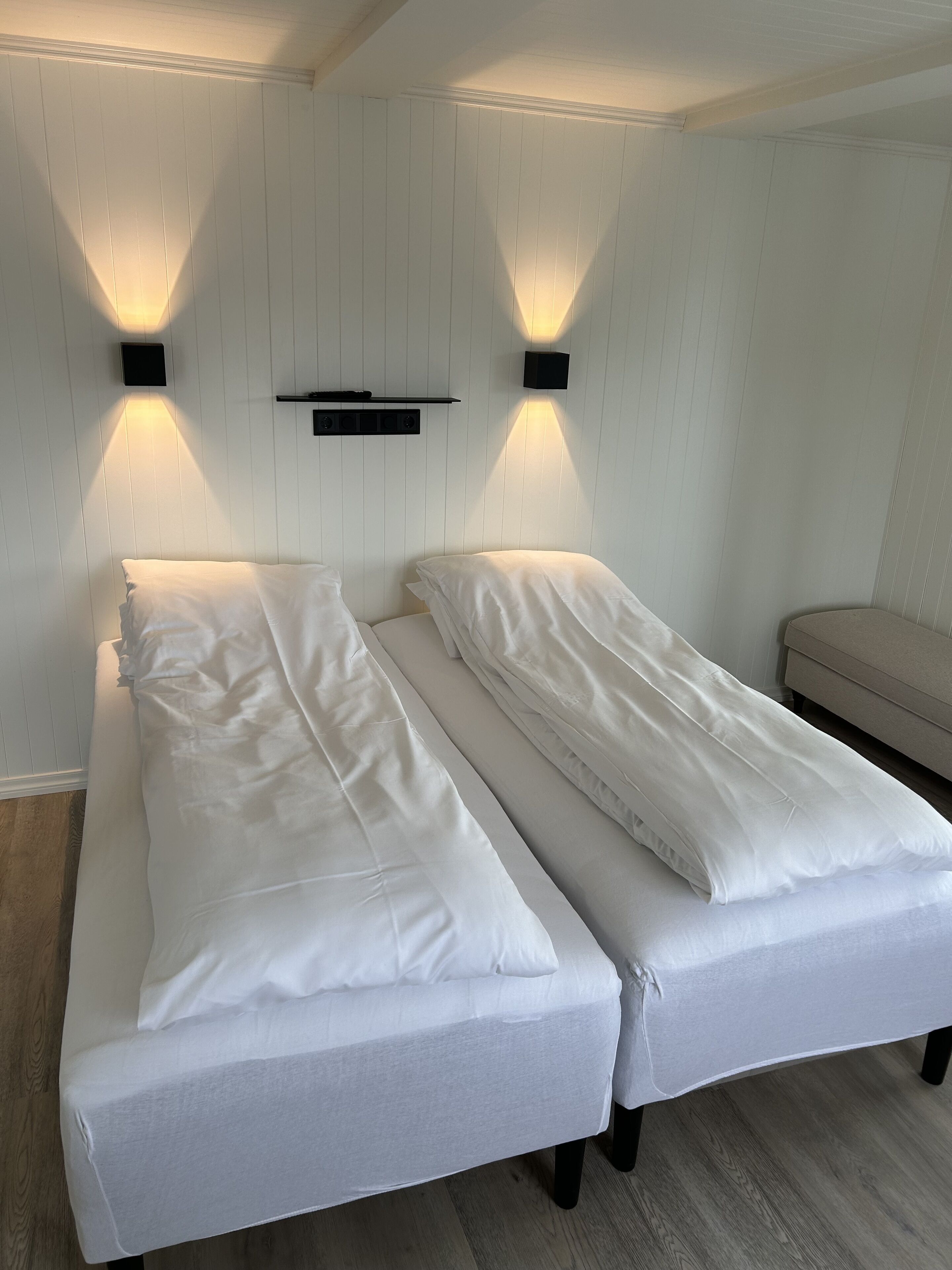 A double bed with white linens and two wall-mounted light fixtures.