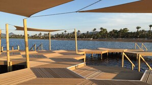 Una terraza de madera con vista al agua y palmeras al fondo.