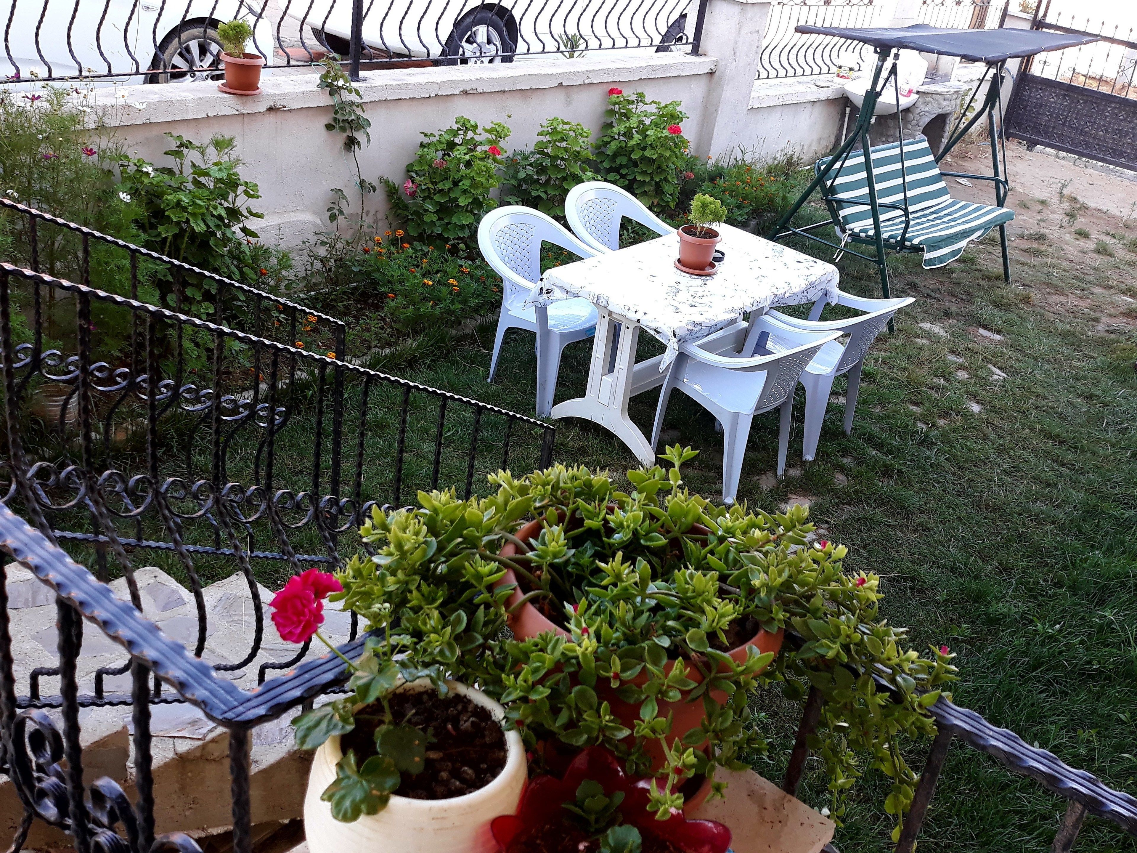 A balcony with a table and chairs, surrounded by potted plants and a garden.
