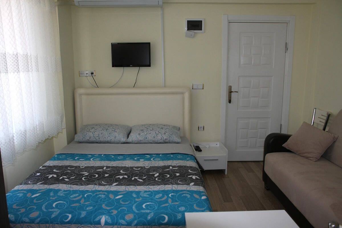 Quarto com cama, televisão, porta e mesa de cabeceira.