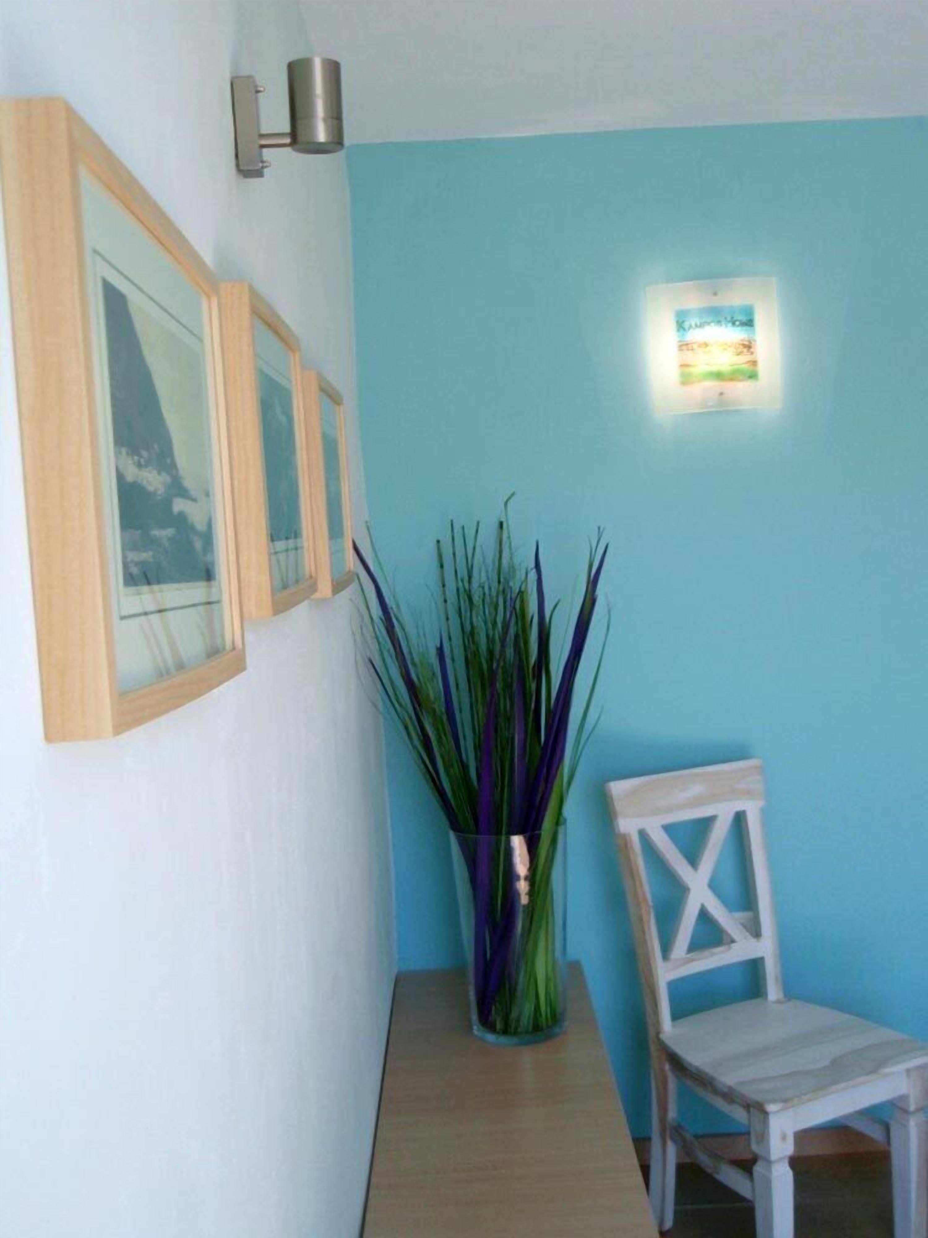 Et værelse med lyseblå væg, et indrammet billede, en vase med grønne planter og en hvid stol.