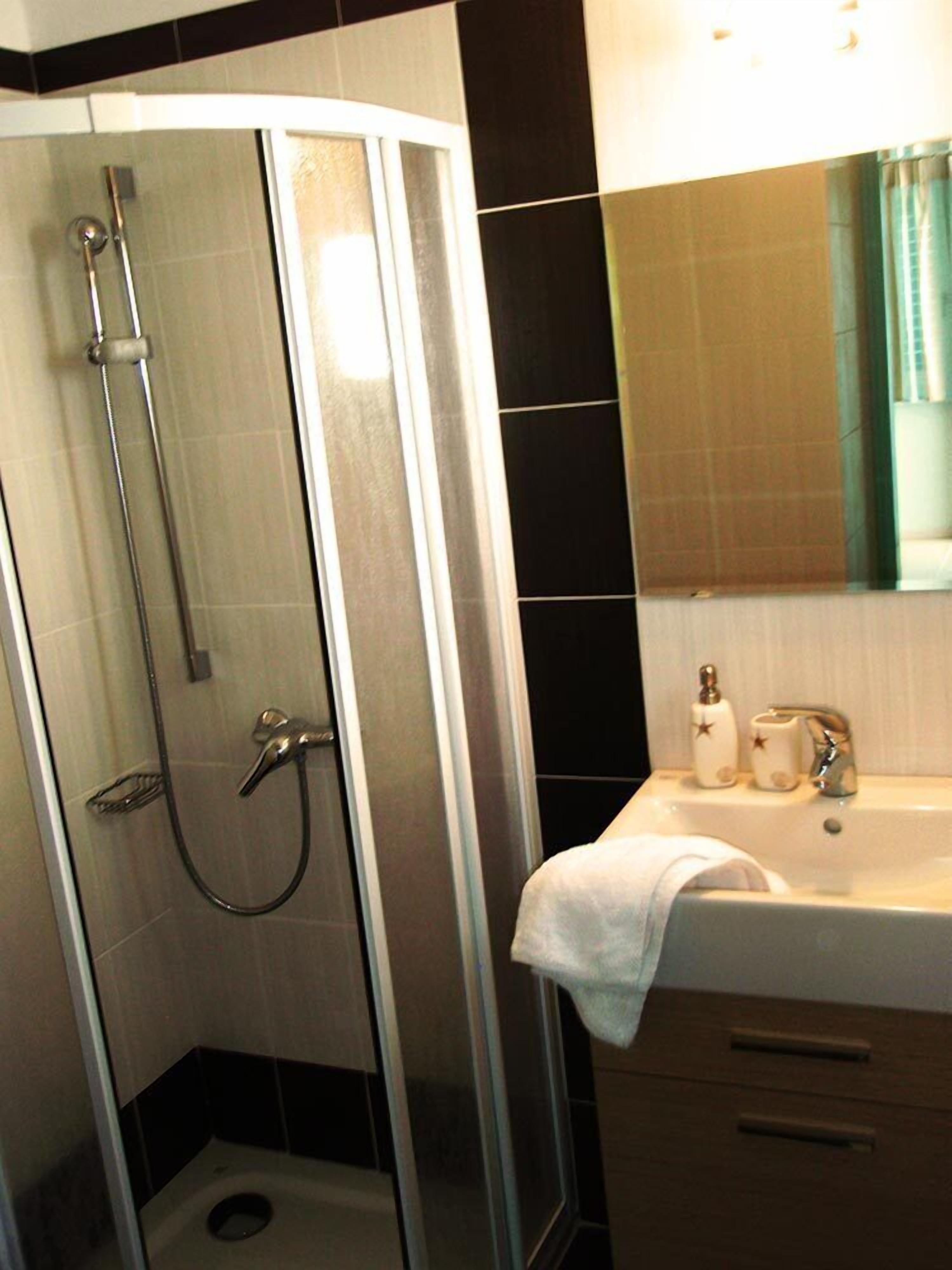 Un baño moderno con ducha de mampara de vidrio, un lavabo con espejo y artículos de aseo.