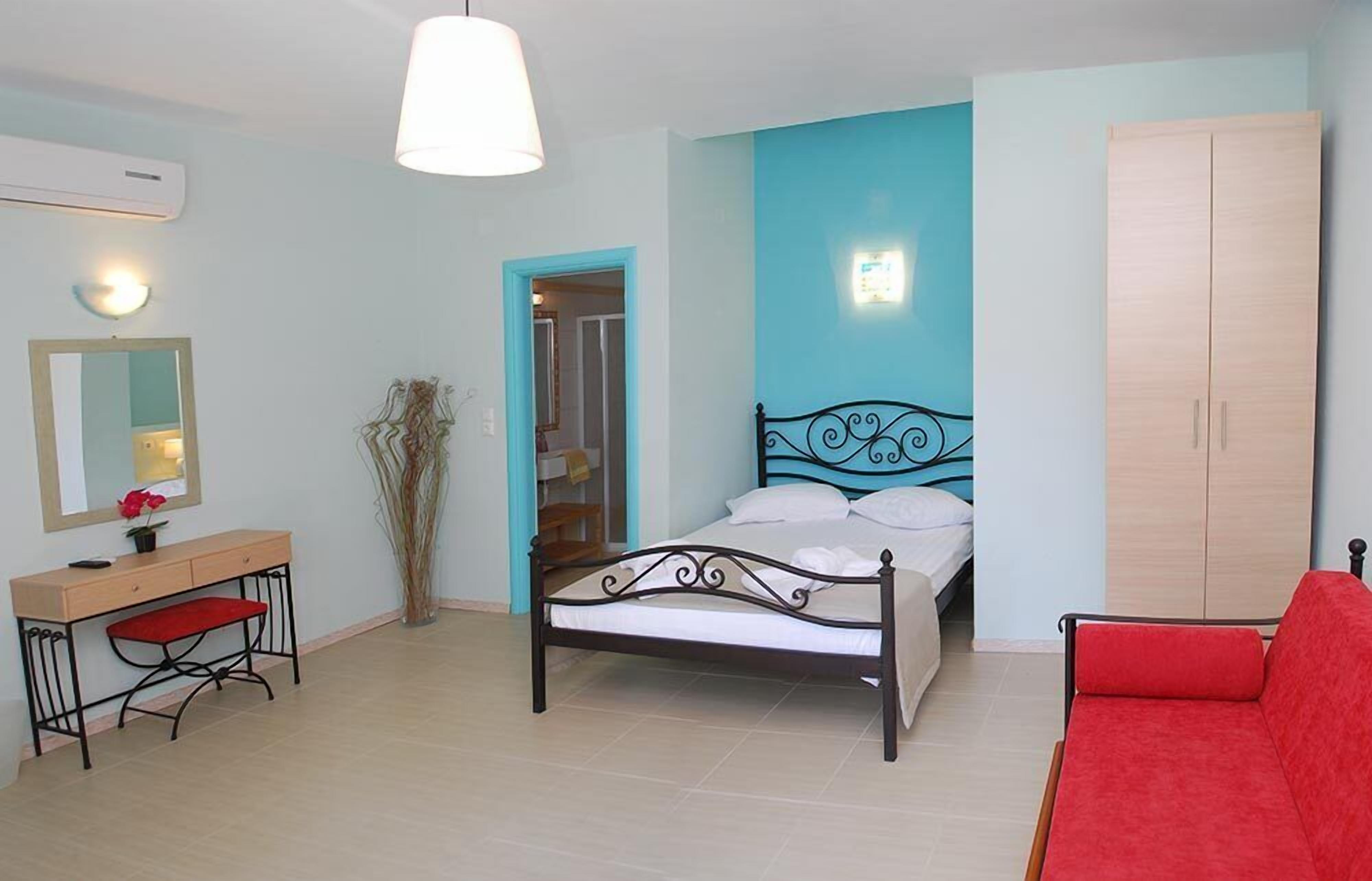 A bedroom with a bed, a desk with a chair, a wardrobe, and a red sofa.
