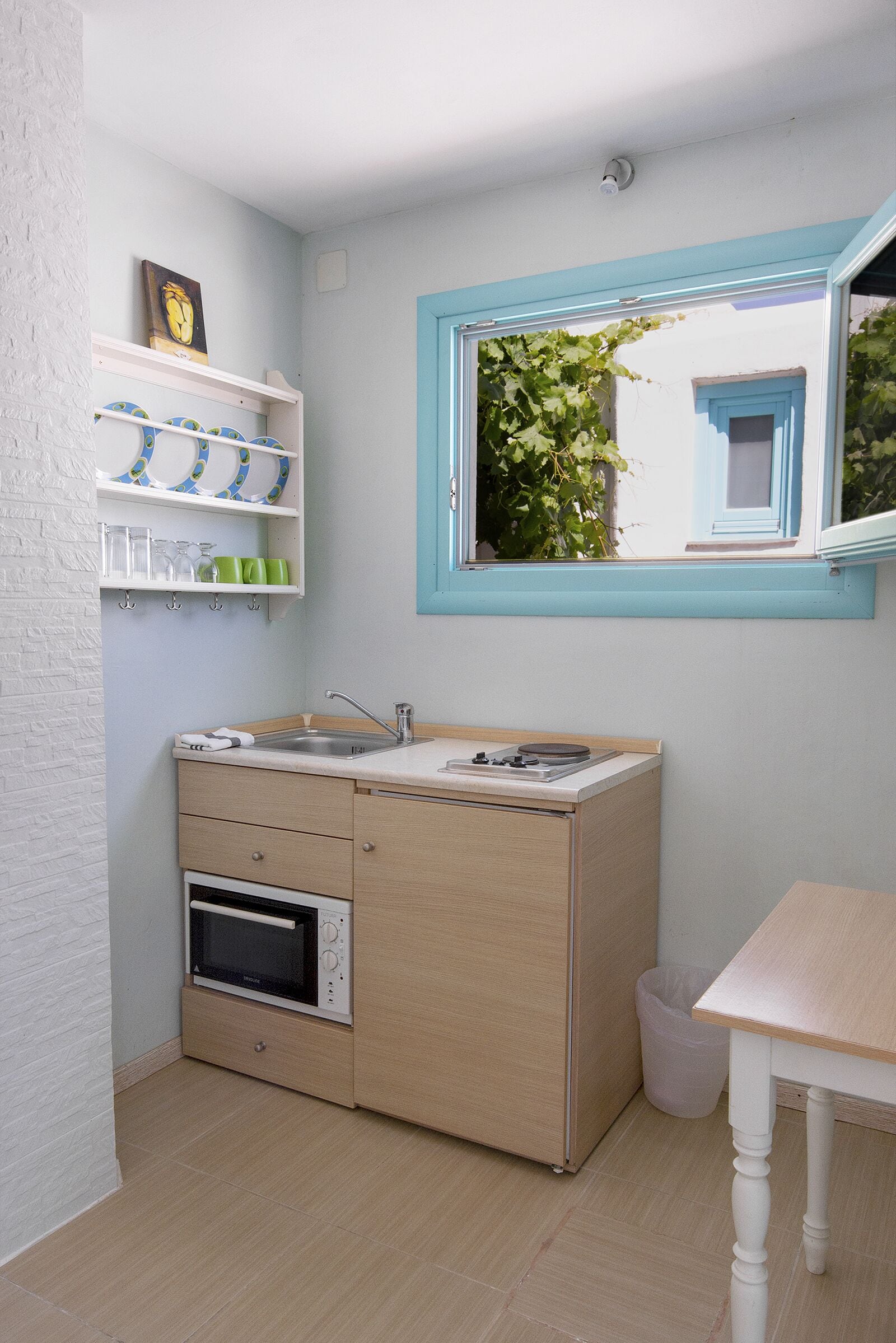 Een compacte keuken met een ingebouwde oven, een spoelbak en een raam met uitzicht op groen.