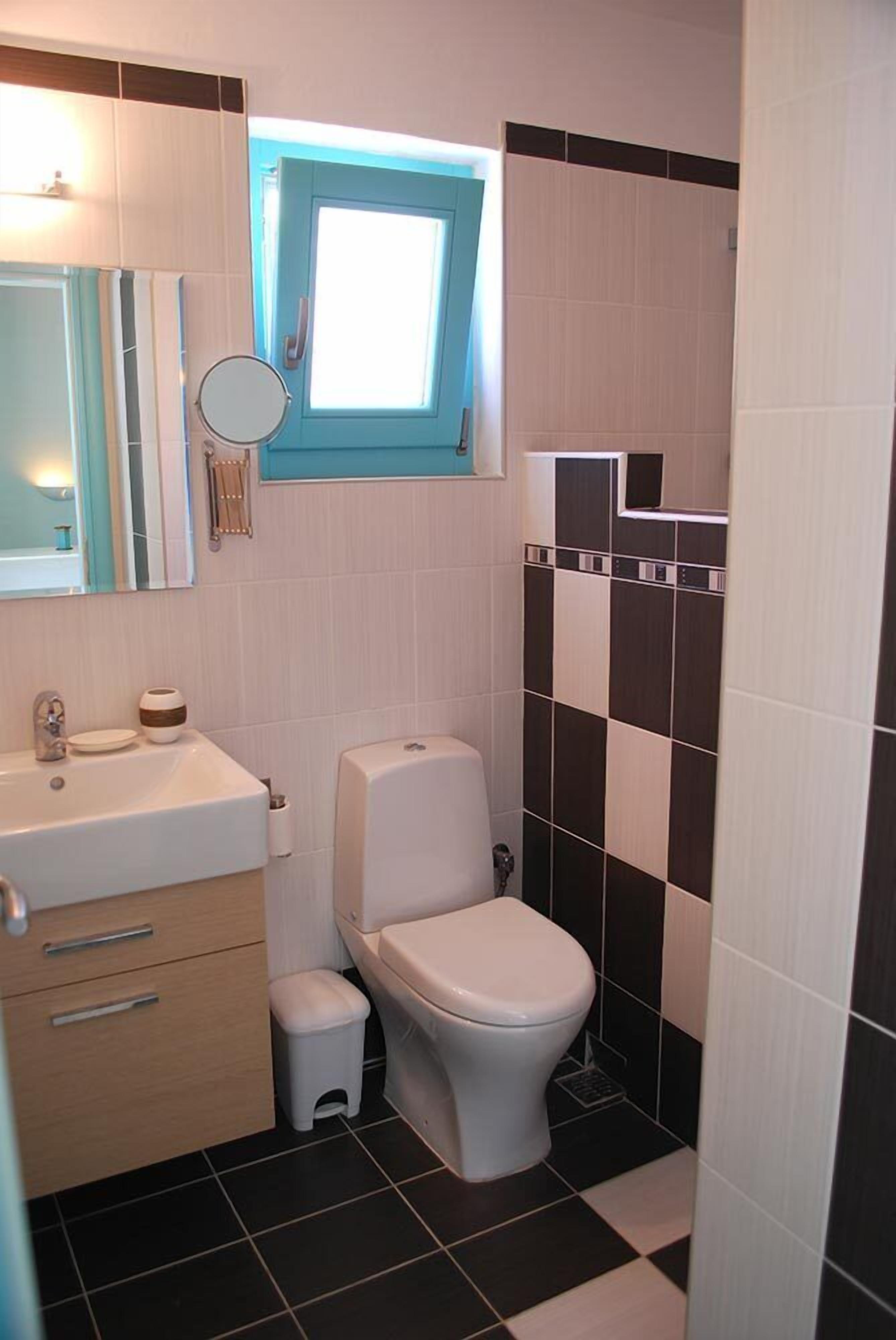 A compact bathroom with a white sink, a mirror, a toilet, and a small window.