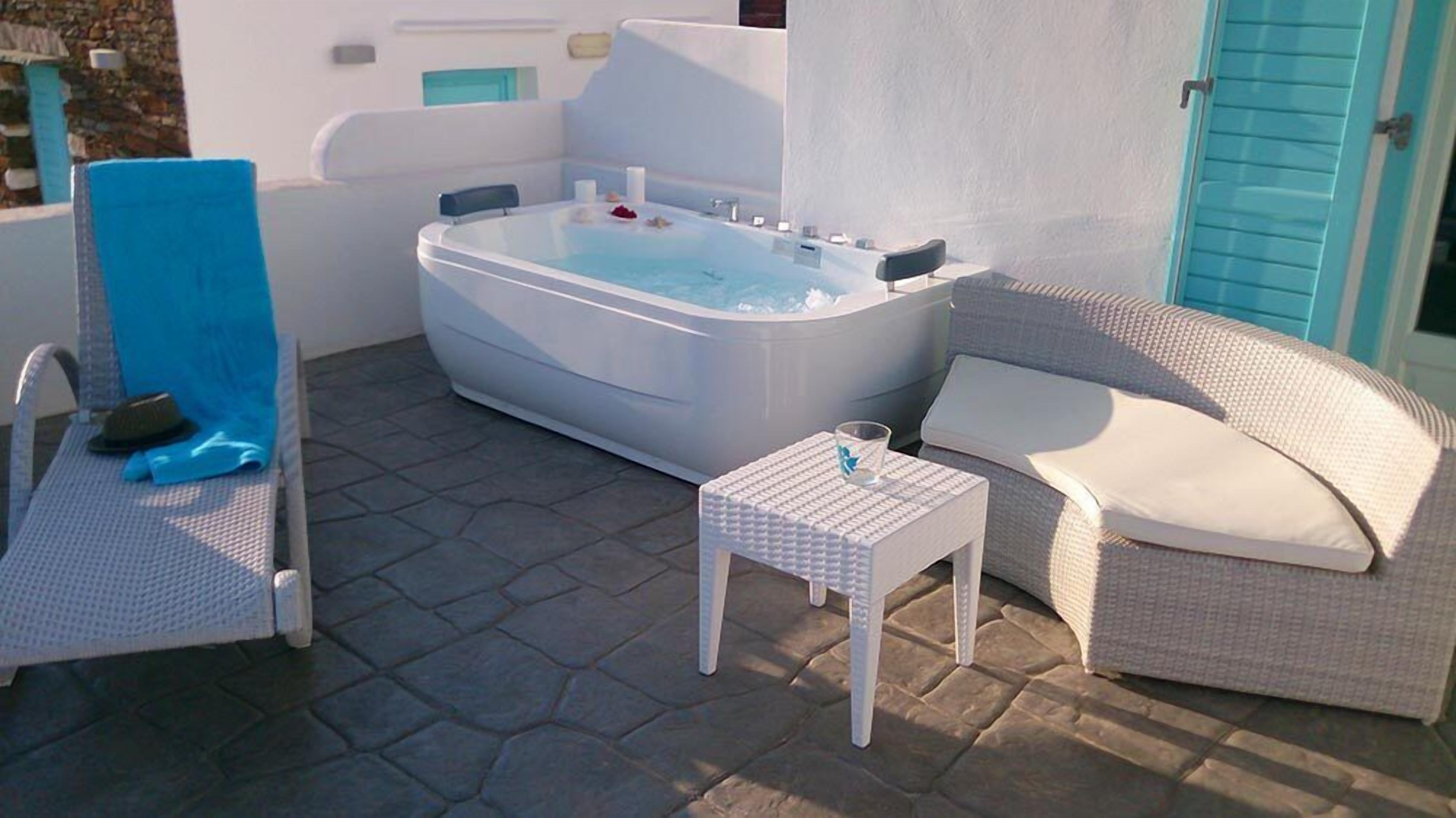 Un jacuzzi con una silla y una mesita, un sofá de mimbre y un patio con suelo de piedra.