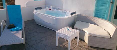 Un jacuzzi con una silla y una mesita, un sofá de mimbre y un patio con suelo de piedra.