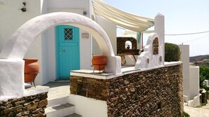 A white building with a turquoise door, stone walls, and terracotta pots.