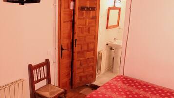 Un dormitorio con dos camas, una silla de madera, un televisor y un baño visible a través de una puerta abierta.