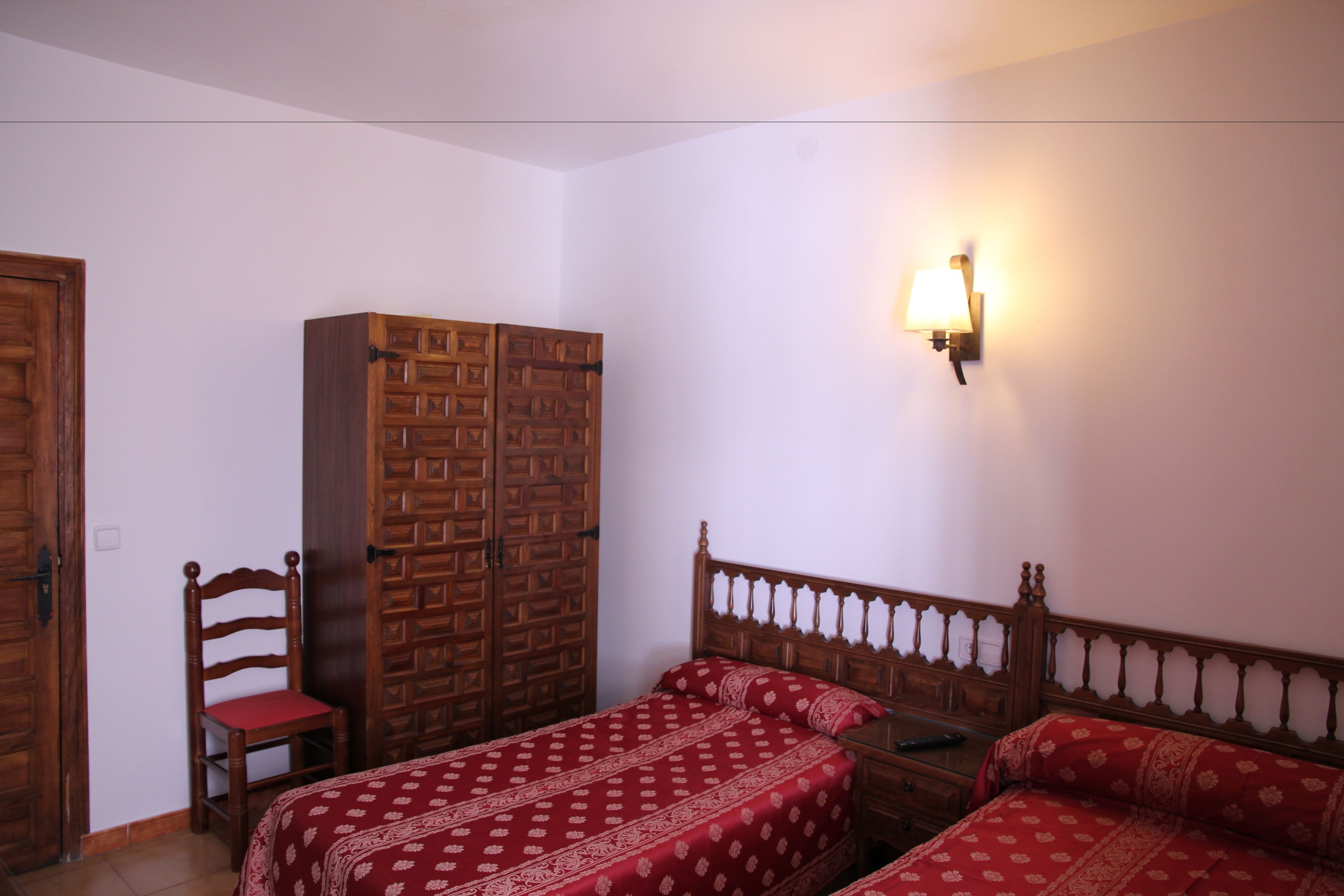 Un dormitorio con dos camas individuales, un armario de madera, una silla y una lámpara de pared.