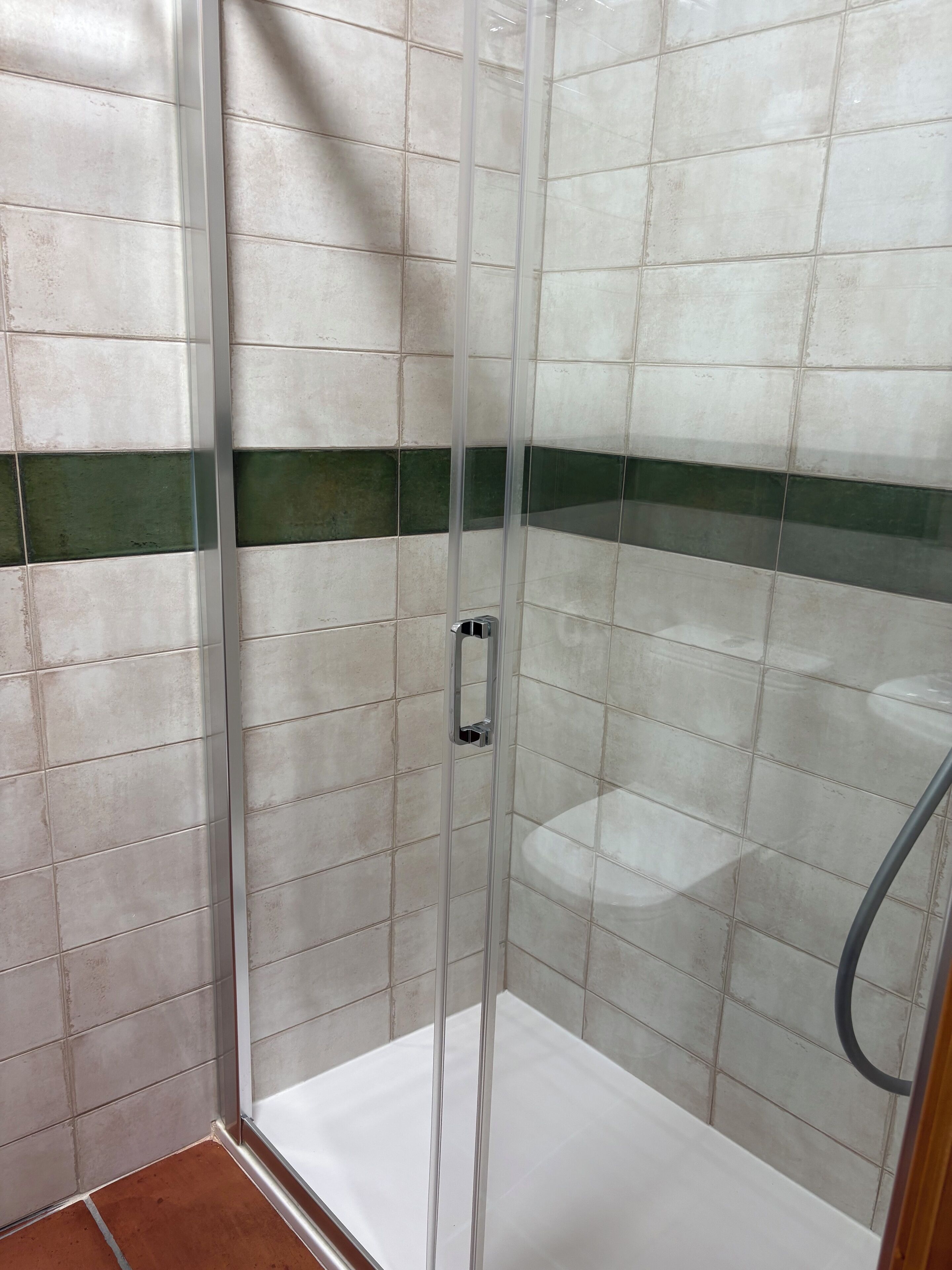A glass-enclosed shower stall with white and green tiles.