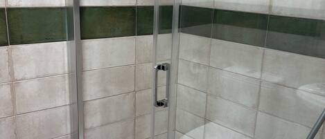 A glass-enclosed shower stall with white and green tiles.