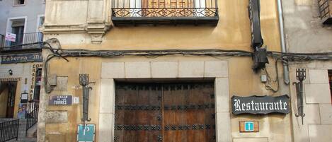 A building with a large wooden door, a balcony with a wrought iron railing, and a sign that reads "Restaurante".