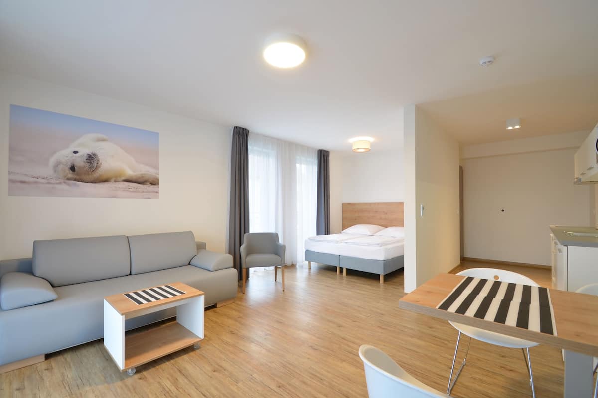 A modern hotel room with a sofa, a bed, a dining table, and a chair.